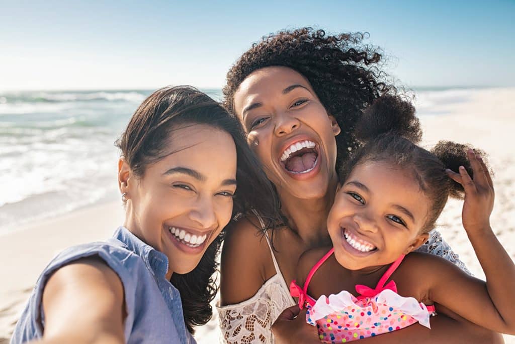 Two women on the beach with their child; they are all laughing